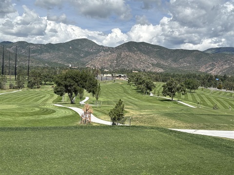 Picture of 3 green fairways, with mow strips, green trees, mountains in the backgournd and blue sky with clouds.
